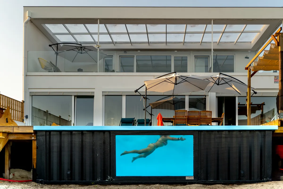 Vista frontal da Casa Aveiro e da piscina com uma pessoa a nadar, vista pela janela subaquática