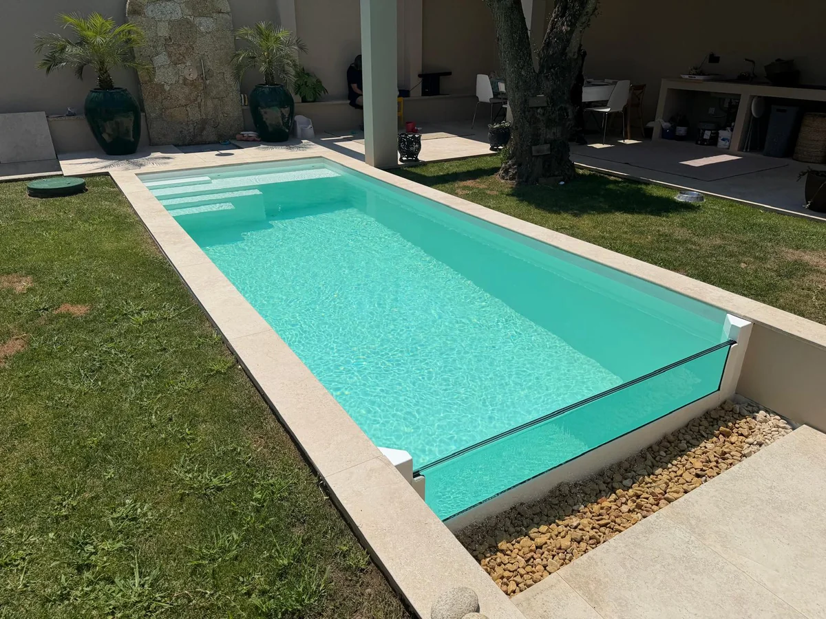 Piscina clara com frente em vidro, água turquesa e relva em redor