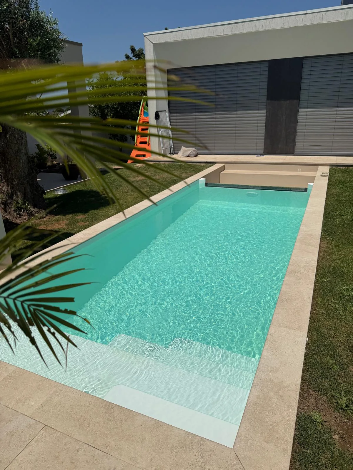 Piscina retangular de bordadura clara junto a uma casa e ao jardim